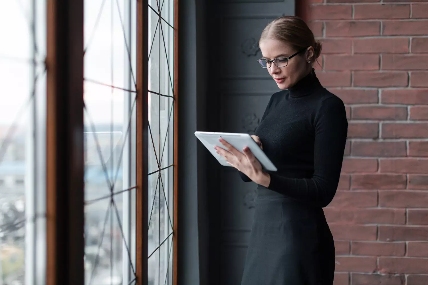 a woman standing in front of a window looking at a tablet