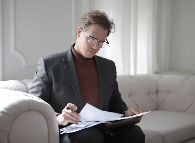 Man in a suit reviewing A5 business documents on a sofa, focusing on financial strategies and AFSL compliance.