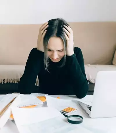 Woman looking stressed with paperwork on table, illustrating common mistakes in AFSL application process.