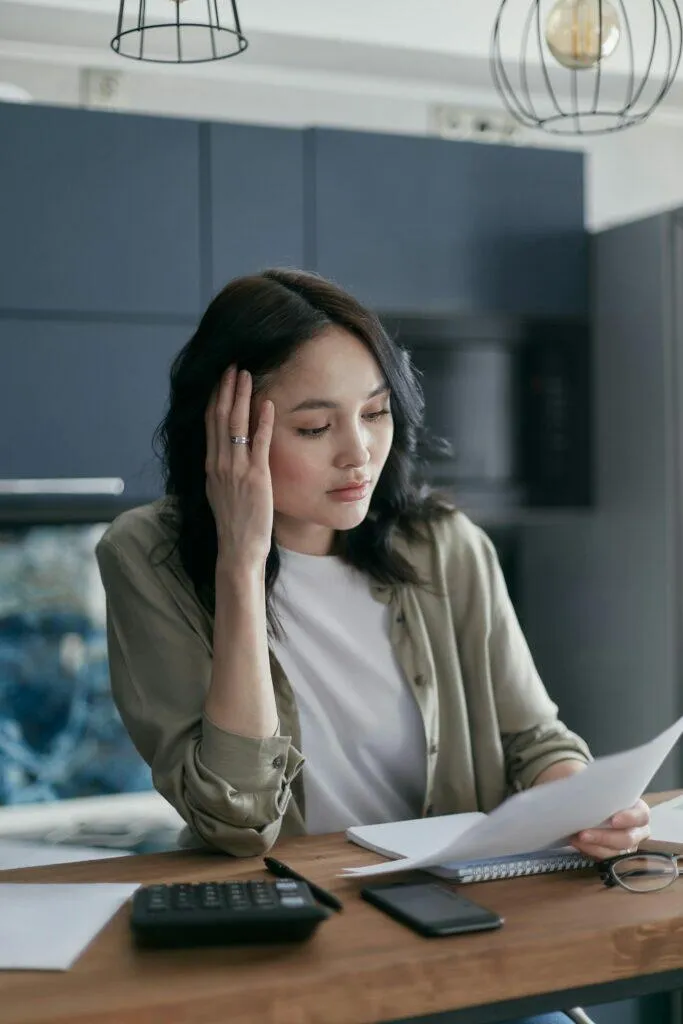 Concerned woman reviewing documents at desk, possibly related to ACL responsible manager qualifications.