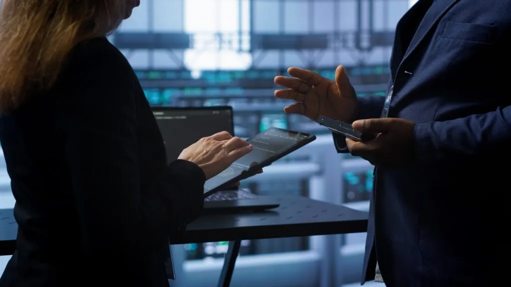 Two professionals discussing information on a laptop and tablet