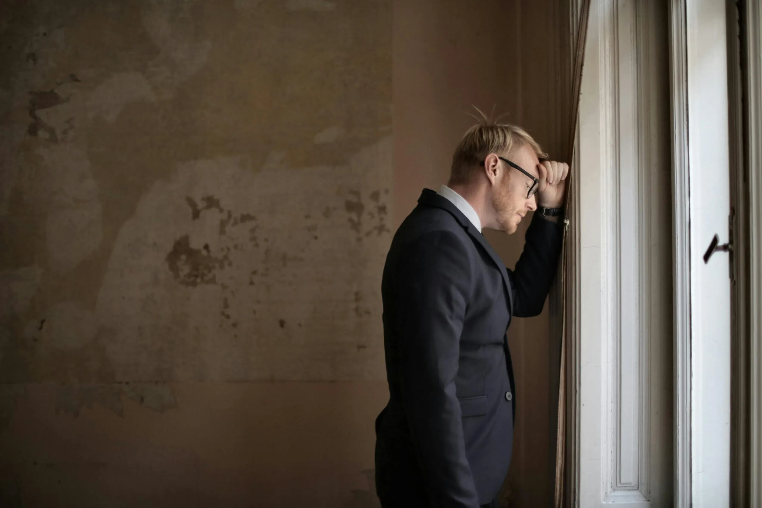 Man in suit looking out a window with a thoughtful expression
