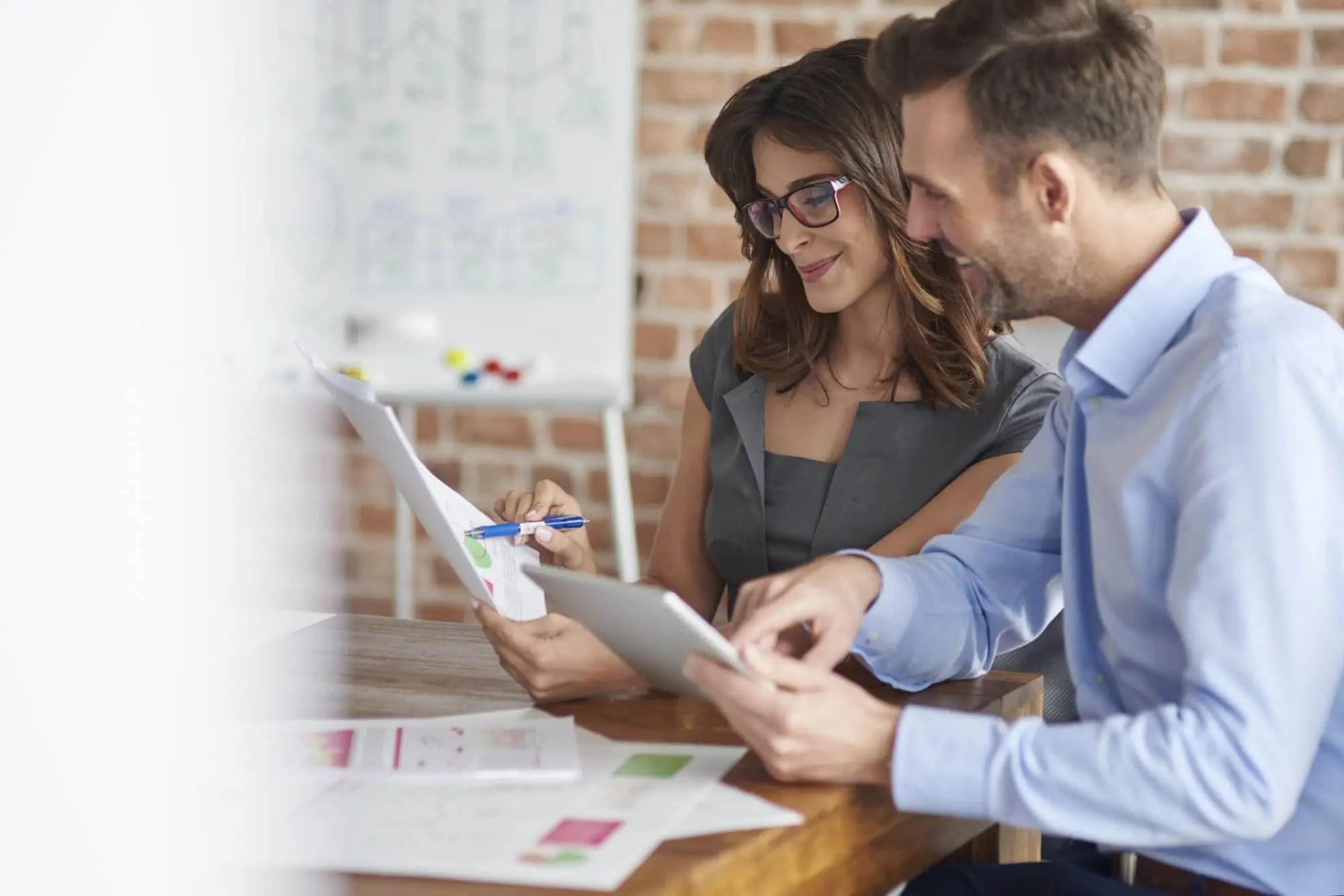 Two business colleagues review financial documents and a tablet, discussing an Australian Financial Services Licence application.