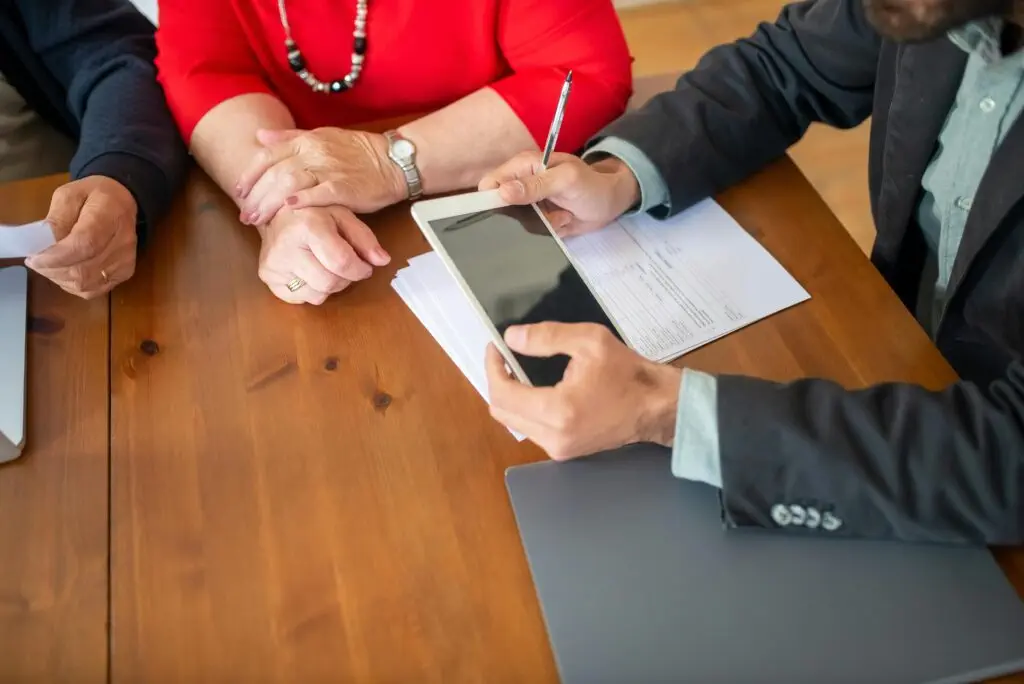 Financial advisor consulting senior couple, reviewing documents and using a tablet. Ensuring AFSL compliance.