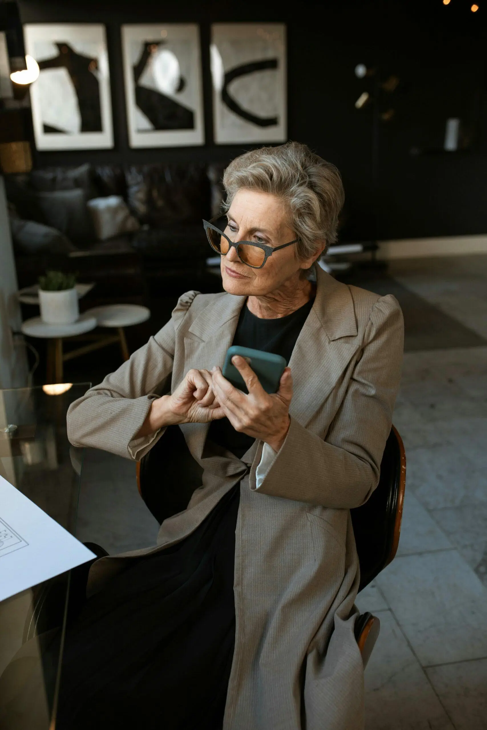 Mature woman in a beige blazer using a smartphone.